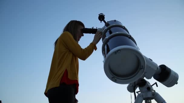 Młoda kobieta, patrząc przez teleskop astronomiczny o niebo wieczorem. - Materiał filmowy, wideo