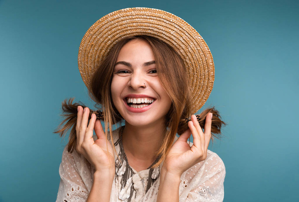 Porträt eines jungen lachenden Mädchens mit Sommermütze auf blauem Hintergrund, das in die Kamera blickt - Foto, Bild