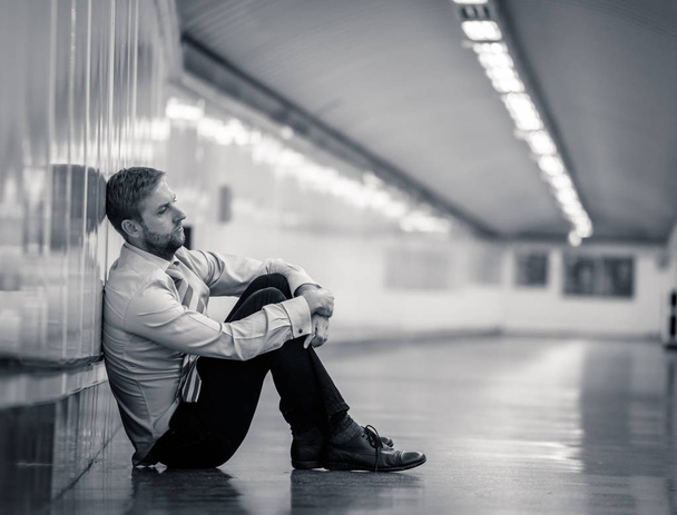 Nuori työtön liikemies, joka kärsii masennuksesta istuessaan maanalaisella kadulla nojaten seinään yksin näyttäen epätoivoiselta henkisessä kivussa.
. - Valokuva, kuva