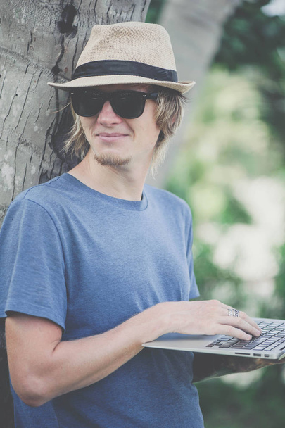 Handsome man in hat working with laptop at the bamboo wall - Fotoğraf, Görsel