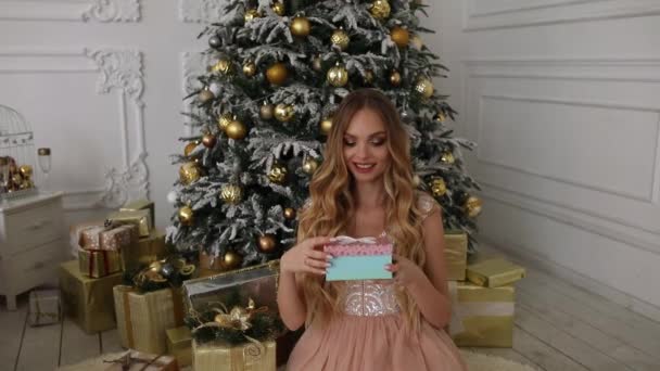 Caja de regalo y mujer sonriente sobre fondo de árbol de Navidad. Bastante rubio con pelo largo y ligero que abre el presente y sonríe
 - Imágenes, Vídeo