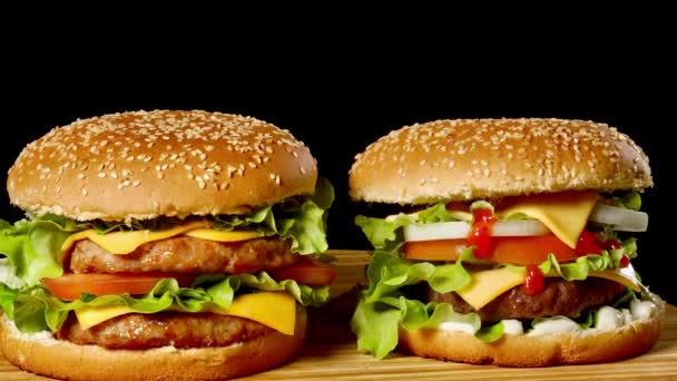 Detail ze dvou chutné hamburgery s housky sezamové otočení na černém pozadí, rychlého občerstvení bezešvé smyčka shot . - Záběry, video