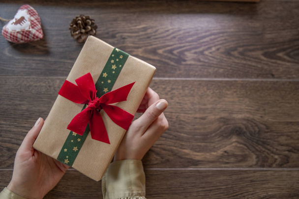 Young woman holding Christmas gift box with red and green ribbon on wooden background - 写真・画像