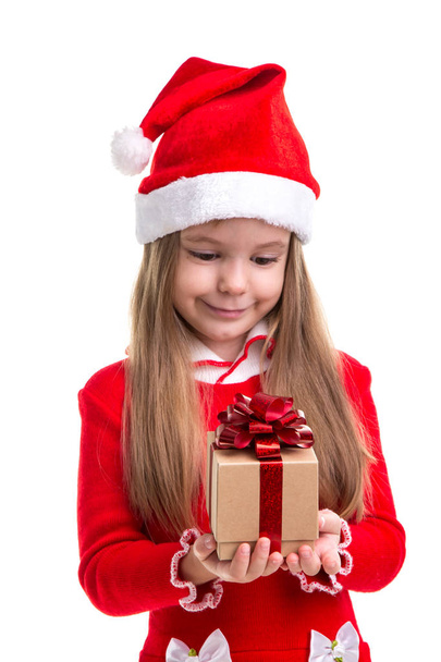 Happy christmas girl holding and lookning at the gift it in the hands, wearing a santa hat isolated over a white background - Фото, изображение