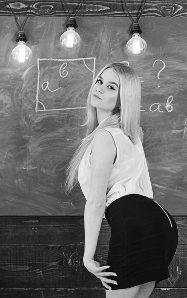Woman with nice buttocks teaching mathematics. Lady sexy teacher in short skirt looking back while explaining formula. Teacher of mathematics writing on chalkboard, rear view. Sexy teacher concept - Foto, immagini