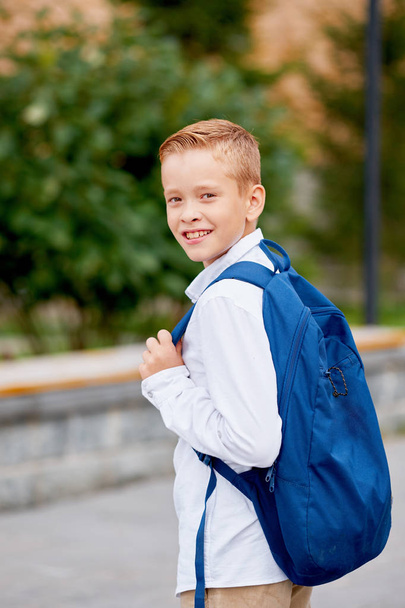 Young elementary schoolboy carrying backpack. Cheerful child standing outdoor - Zdjęcie, obraz