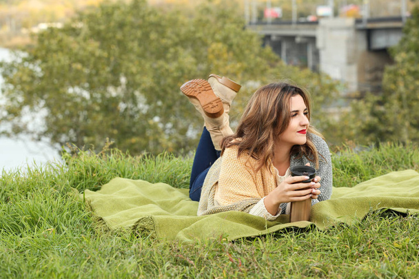 Hermosa mujer joven con termos descansando en cuadros al aire libre
 - Foto, Imagen