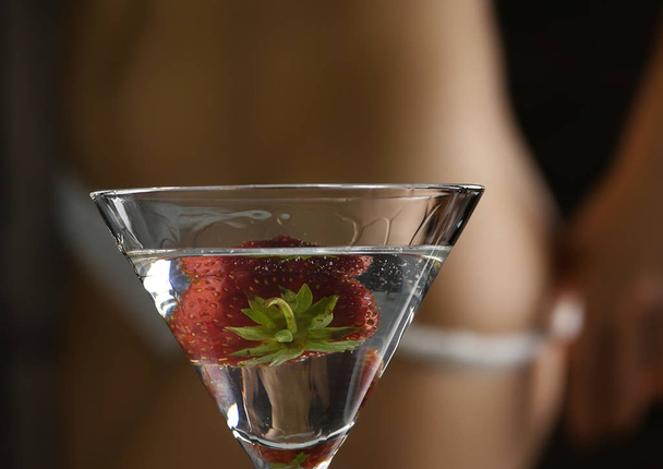 cocktail with strawberry and blured female buttocks in white panties in a dark background. dating and party concept. - 写真・画像