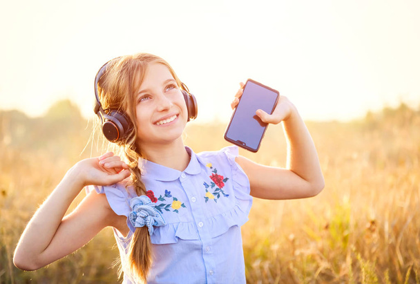 Smiling girl hold smartphone and listening to music with raised hands - Φωτογραφία, εικόνα