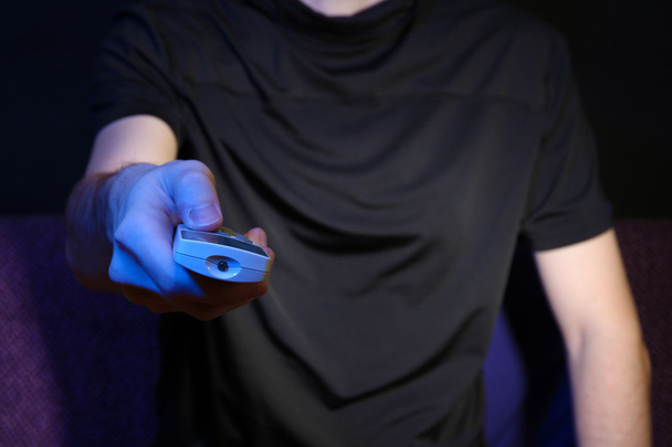 Man hand holding a TV remote control, on dark background - Foto, Imagen