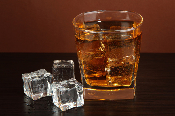 Glass of whiskey and ice on brown background - Фото, зображення