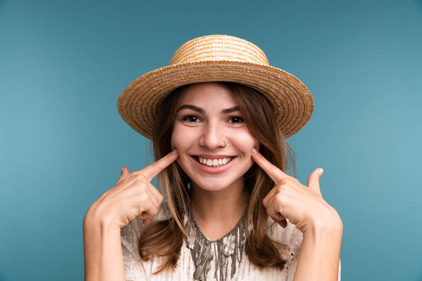 Portrait of a young happy girl in summer hat isolated over blue background, looking at camera - Fotografie, Obrázek
