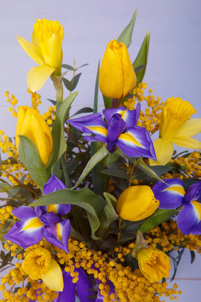 Flower arrangement bouquet of blue iris, white tulip, yellow mimosa and narcissus against a gray background. For decoration, web design. Close up. - Photo, Image