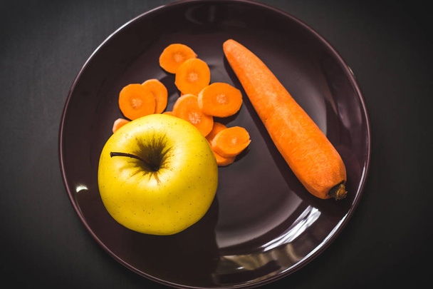 Food photo of yellow apple with a carrot near it on a dark plate - Fotoğraf, Görsel