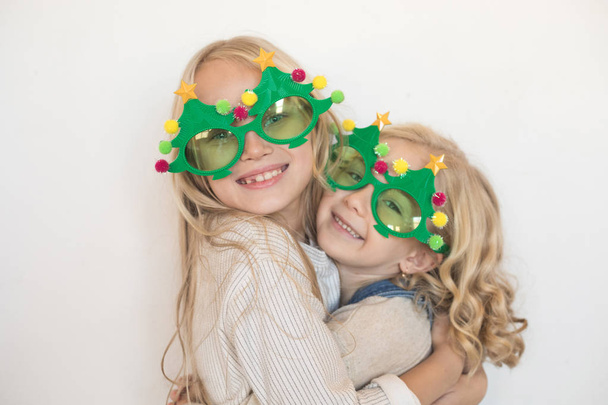 Two little girls hugging in funny glasses in the form of Christmas trees. - Foto, Imagem
