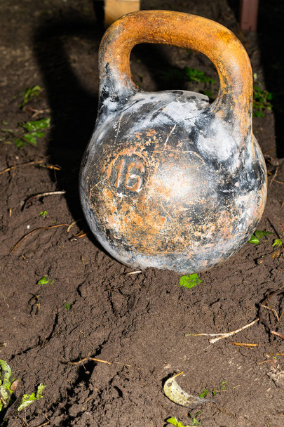 An old cast-iron sports weight on the ground. Inventory for power sport of bodybuilding. - Photo, Image