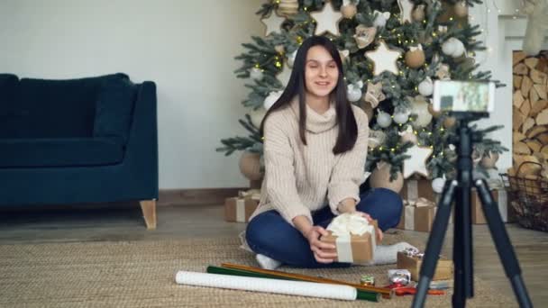 Creative young lady is recording video for online vlog about gift-wrapping for Christmas holidays. Girl is showing wrapping paper, boxes, ribbons and scissors. - Filmagem, Vídeo