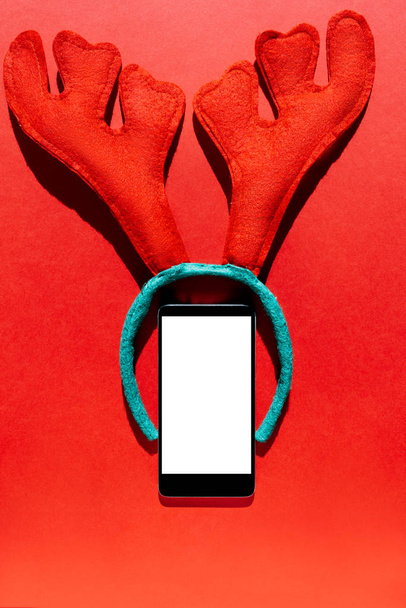 Cep telefonu ve geyik boynuzları, kırmızı Noel arka plan ile kafa bandı. yukarıdan - Fotoğraf, Görsel