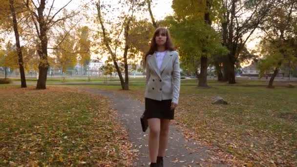 iş kadını siyah evrak çantası ile sonbahar park yolunda gider - Video, Çekim