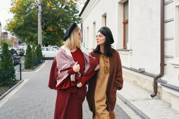 Carefree fashionable women models in elegant autumn clothes and glasses. Young fashion girls in stylish woven wool clothes and hats over urban city background, autumn portrait.  - Photo, Image