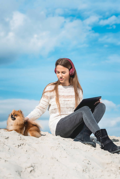 14 anos menina em um fone de ouvido sem fio ouvindo uma música de um telefone inteligente em uma praia. contra um céu azul. de perto
 - Foto, Imagem