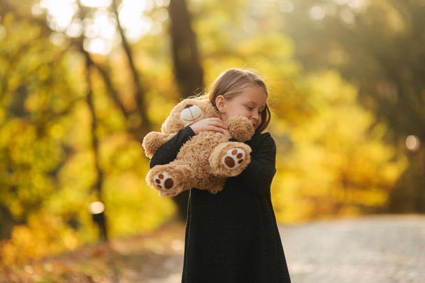 Portrait of little girl which hold teddy bear in hands. Happy child in the park. Beautiful girl model smile to camera - Photo, Image