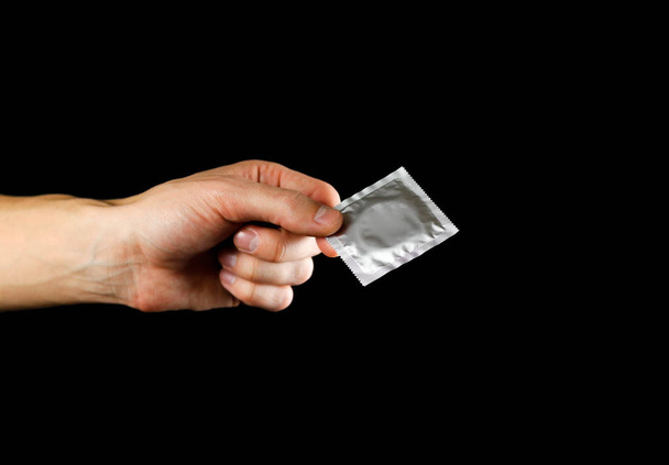 Hand holding a condom. Close up. Isolated on black background. - Фото, изображение