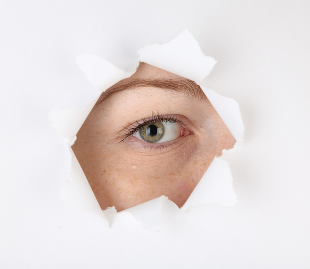 Female eye looking through hole in sheet of paper - Zdjęcie, obraz