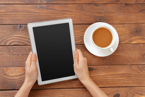 Girl hands with digital tablet and cup of coffee on a wooden table - Foto, Bild