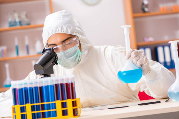 Laboratuvarda çalışan koruyucu elbise giyen genç bir biyokimyacı. - Fotoğraf, Görsel