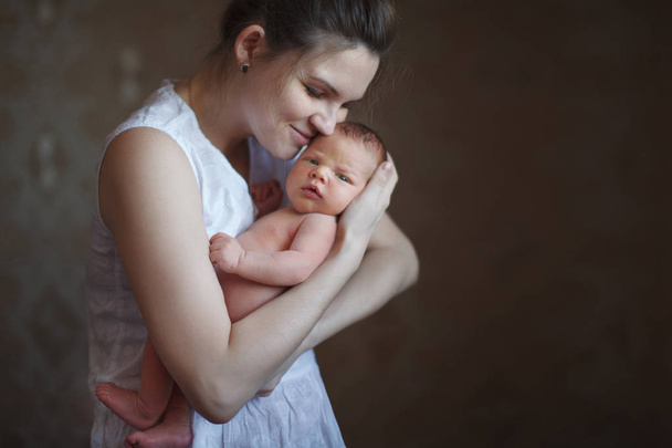 Jovem mãe bonito segurando um filho recém-nascido em seus braços e sorrindo. O conceito de uma infância feliz, maternidade, amamentação
. - Foto, Imagem