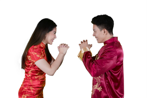 Imagem de jovem casal vestindo vestido tradicional chinês, dando gong xi fa chai cumprimentos no estúdio
 - Foto, Imagem