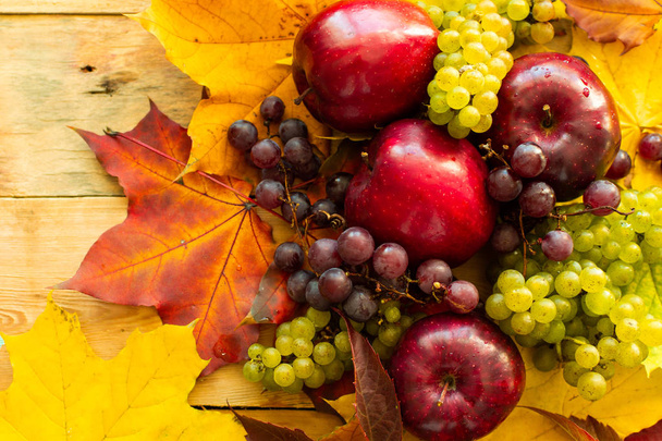 Draufsicht auf rote saftige reife Äpfel mit Trauben und Herbst-Ahornblättern auf Holzgrund - Foto, Bild