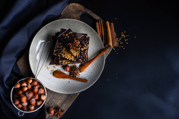 Donkere chocoladestukjes geplet op donkere houten tafel, specerijen zoals een kaneel en anijs ster als een culinair concept met kopie ruimte, bovenaanzicht - Foto, afbeelding
