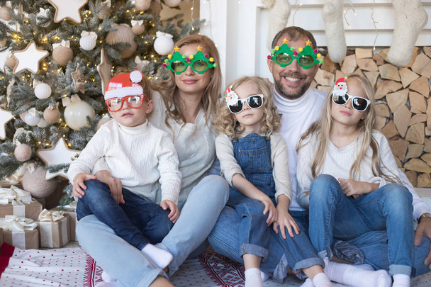 Happy family sitting near the Christmas tree in funny glasses. - Photo, image