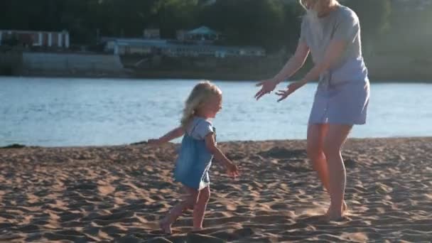 Mom and girl playing on the beach of the river at sunset. - Кадри, відео