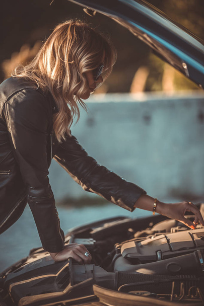 Photo of side of young woman near broken car with open hood - Фото, изображение