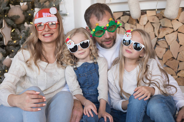 Happy family sitting near the Christmas tree in funny glasses. - Fotografie, Obrázek