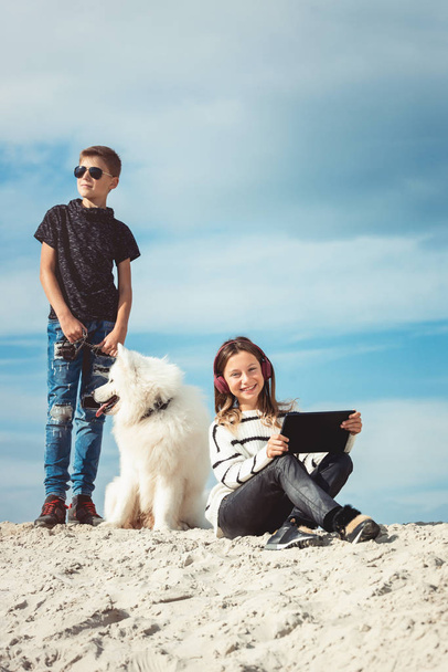 Feliz niño de 11 años consu raza de perro Samoyed en la orilla del mar contra un cielo azul de cerca. Los mejores amigos descansan y se divierten de vacaciones, juegan en la arena
 - Foto, imagen