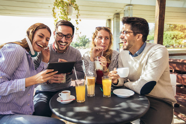 Skupina čtyř přátel společně baví na kávu. Dvě ženy a dva muži v kavárně mluví směje a používání digitálních tabletu. - Fotografie, Obrázek