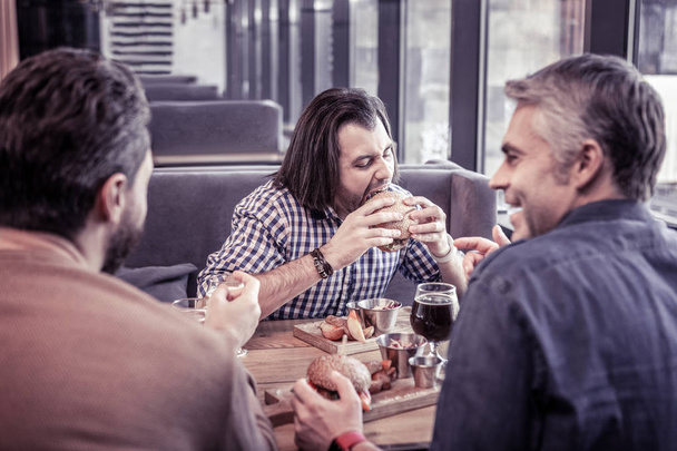 Concentrated brunette man eating burger with pleasure - Foto, Bild