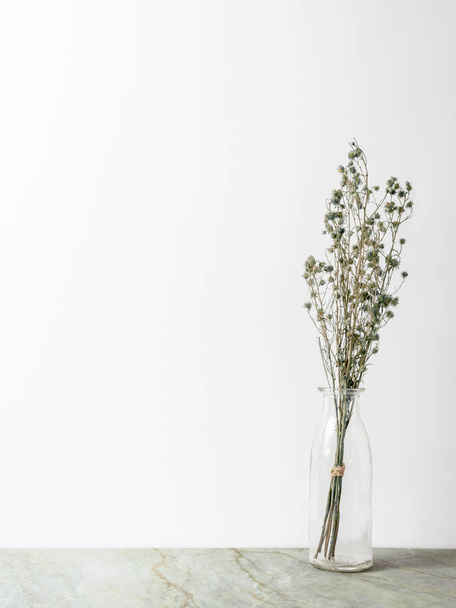 Μπουκέτο από αποξηραμένα και μαραμένα πράσινα λουλούδια γυψοφύλλι σε γυάλινη φιάλη σε ματ μαρμάρινο πάτωμα και λευκό φόντο με αντίγραφο χώρου - Φωτογραφία, εικόνα