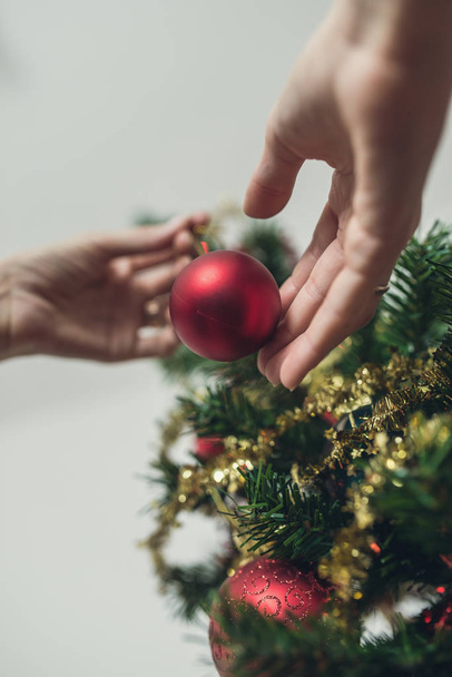 Vista de ángulo bajo de la mano femenina colocando bola roja de vacaciones en el árbol de Navidad. Con efecto de filtro retro
. - Foto, Imagen
