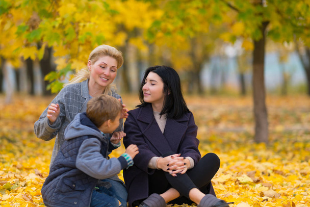 A same sex female couple with their son in a happy family portrait at a city park with yellow fall leaves. - Foto, Imagem