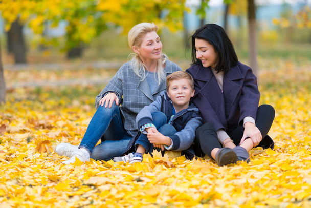 A happy, content same sex female couple and their son in a happy family theme with yellow fall leaves. - Фото, зображення