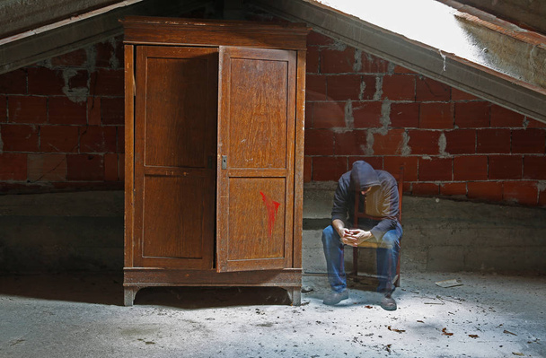 unavený muž jako duše sedí na židli v podkroví a dřevěnou šatní skříň - Fotografie, Obrázek