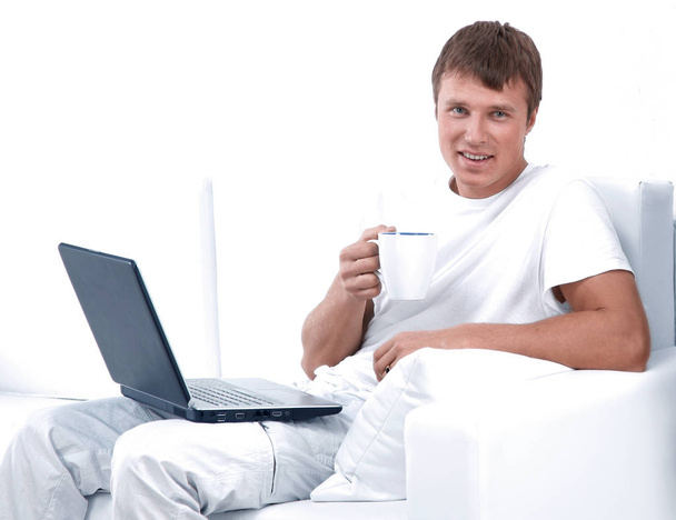 Young man sitting on sofa with laptop and a cup of coffee - Foto, afbeelding