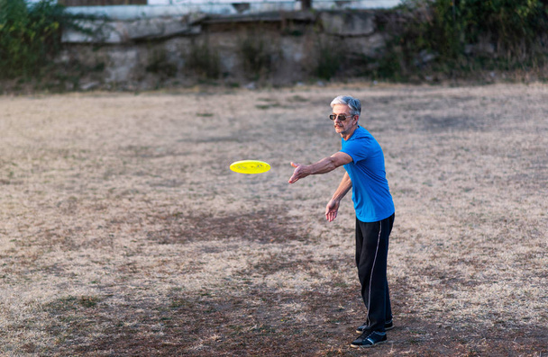 Vanhempi mies leikkimässä frisbeetä puistossa ulkona
 - Valokuva, kuva