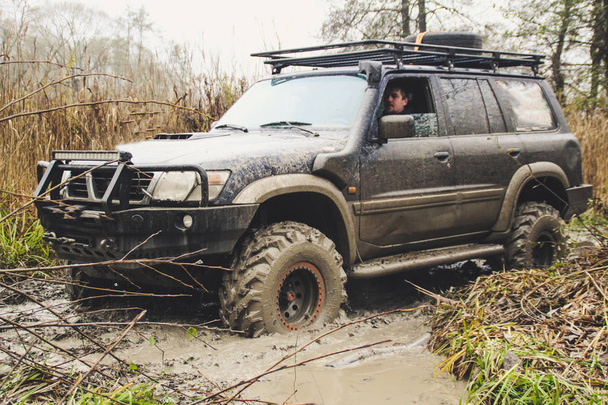 El coche todoterreno atraviesa grandes pantanos. Shrazjuk después de la lluvia. Un camino difícil. Gory Ruedas sucias
. - Foto, Imagen