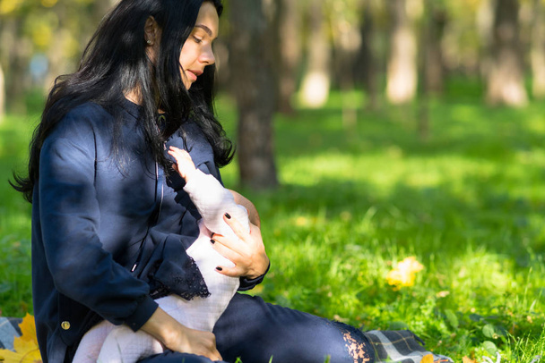 A tired mother discreetly breastfeeding her baby in lush city park. - 写真・画像